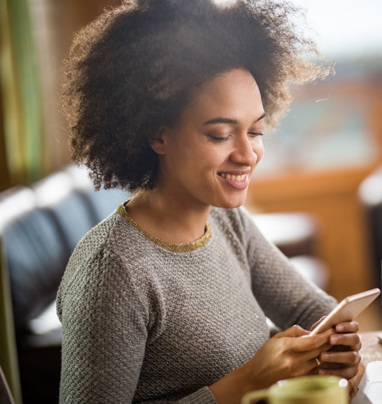 A woman sits and smiles while looking at her phone